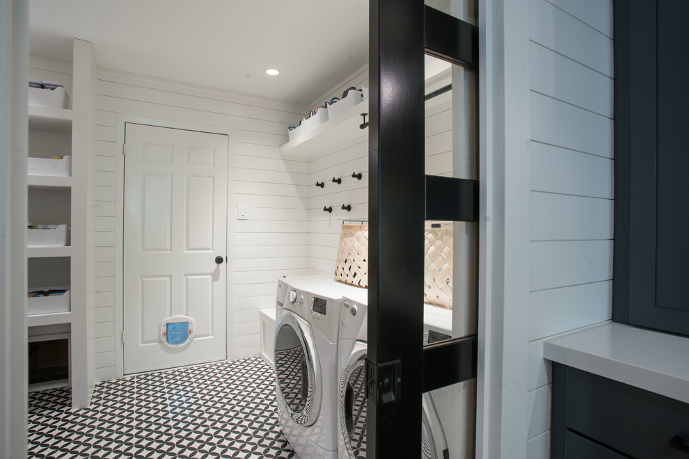 Inspiration for a mid-sized country utility room in Austin with shaker cabinets, white cabinets, white walls, concrete floors, a side-by-side washer and dryer, black floor, white splashback, shiplap splashback and wood walls.