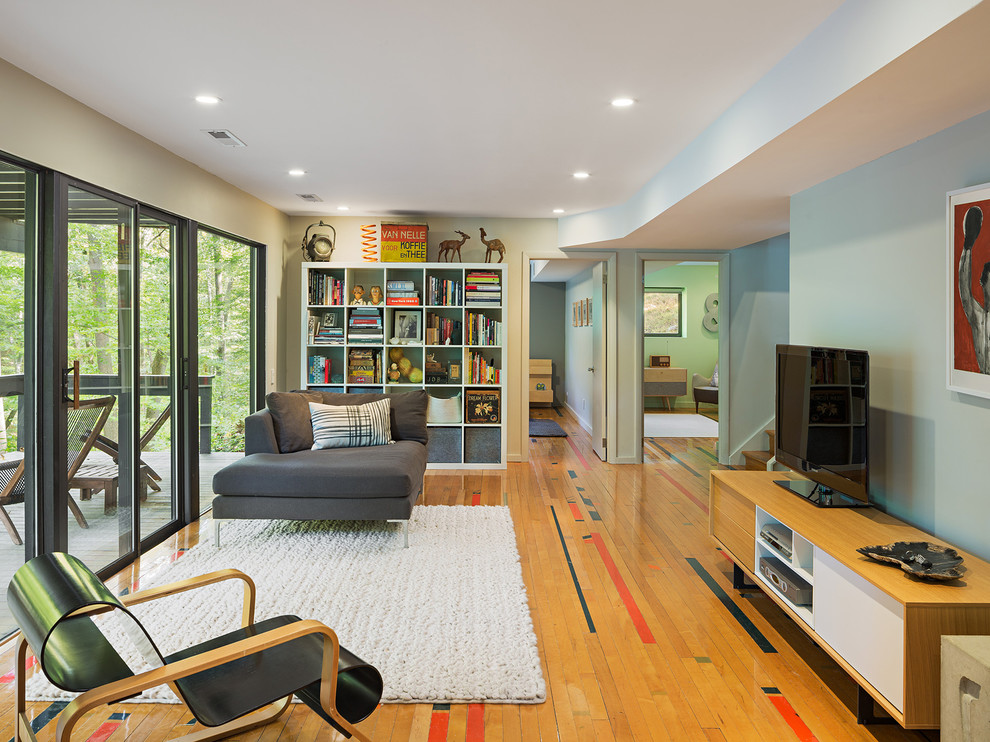 This is an example of a contemporary family room in Philadelphia with a freestanding tv, multi-coloured walls, light hardwood floors and brown floor.