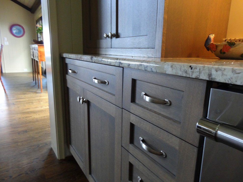 Mid-sized transitional l-shaped dark wood floor eat-in kitchen photo in Charlotte with an undermount sink, shaker cabinets, gray cabinets, granite countertops, white backsplash, stainless steel appliances and an island