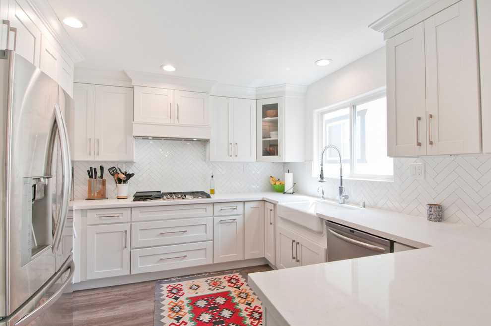 Photo of a mid-sized transitional u-shaped separate kitchen in Los Angeles with a farmhouse sink, shaker cabinets, white cabinets, quartzite benchtops, white splashback, porcelain splashback, stainless steel appliances, dark hardwood floors, a peninsula, grey floor and white benchtop.