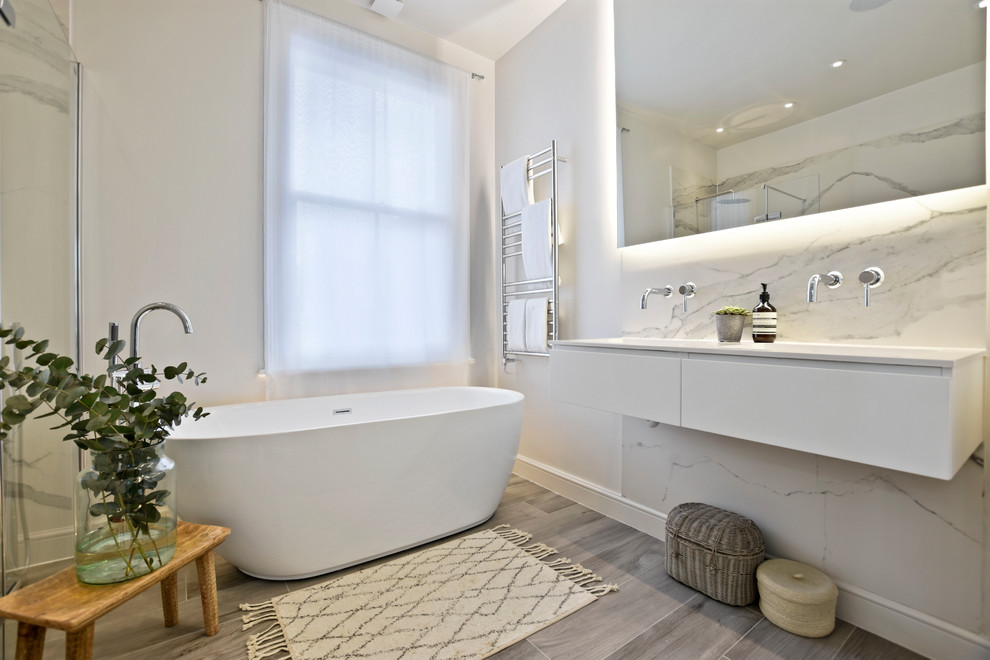 This is an example of a mid-sized contemporary master bathroom in Other with flat-panel cabinets, white cabinets, a freestanding tub, marble, white walls, a wall-mount sink, grey floor, black and white tile and white benchtops.