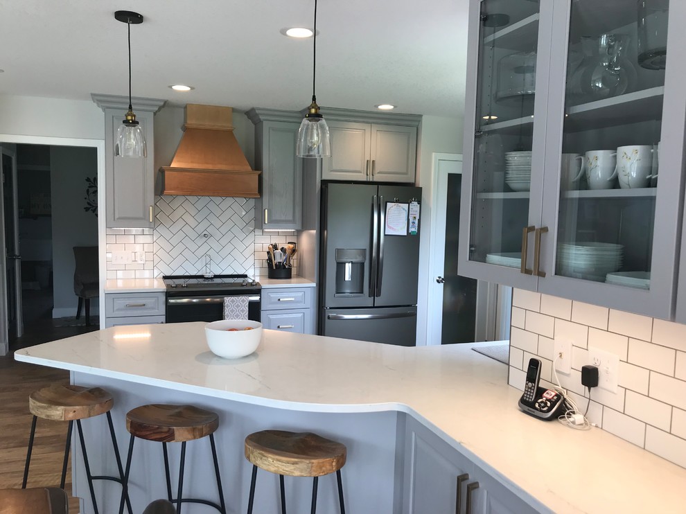 Example of a mid-sized transitional u-shaped vinyl floor and brown floor enclosed kitchen design with an undermount sink, raised-panel cabinets, gray cabinets, quartz countertops, white backsplash, ceramic backsplash, a peninsula and white countertops