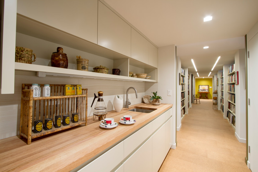 This is an example of a small midcentury galley kitchen pantry in Philadelphia with an undermount sink, flat-panel cabinets, white cabinets, wood benchtops, white splashback, porcelain splashback, stainless steel appliances, cork floors, no island, multi-coloured floor and brown benchtop.