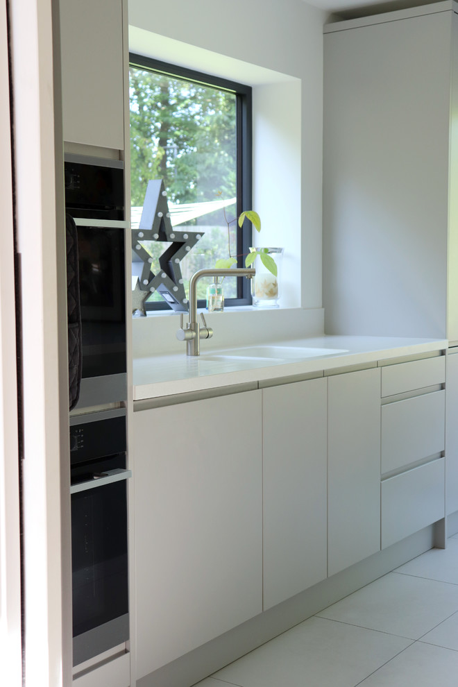 Inspiration for a large contemporary single-wall eat-in kitchen in Hertfordshire with a drop-in sink, flat-panel cabinets, grey cabinets, solid surface benchtops, white splashback, ceramic floors, with island, grey floor and white benchtop.