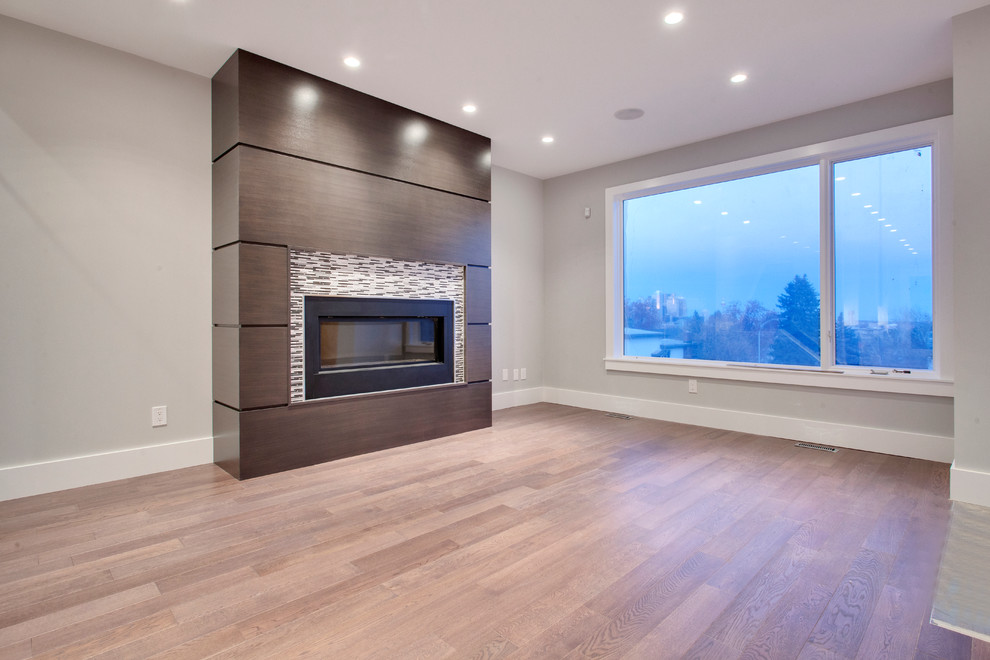 Small modern living room in Calgary with grey walls, medium hardwood floors, a standard fireplace, a tile fireplace surround and a freestanding tv.