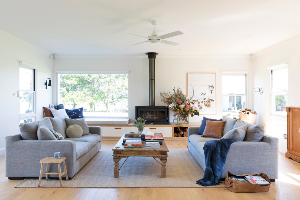 This is an example of a large country open concept living room in Wollongong with a library, white walls, light hardwood floors, brown floor, a wood stove and a metal fireplace surround.