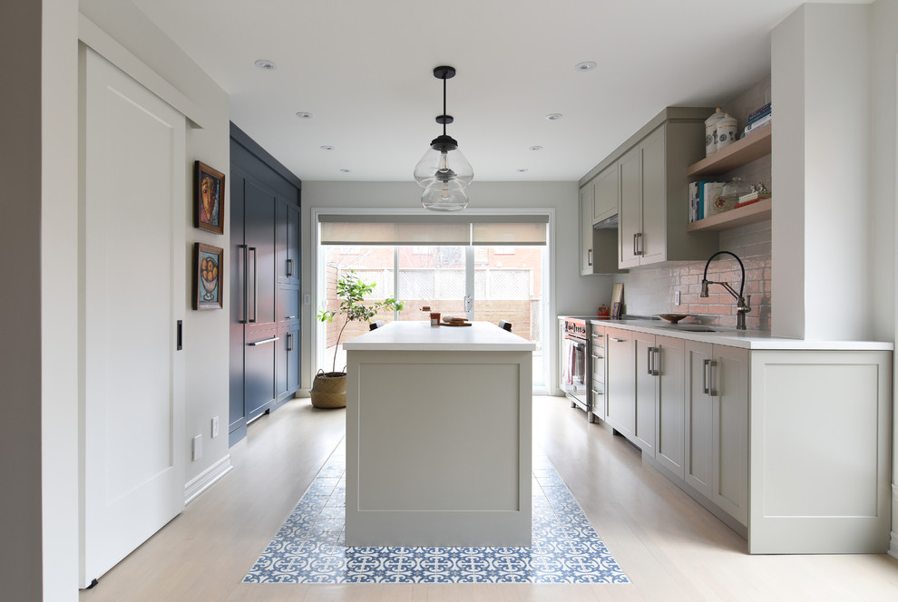 Mid-sized transitional galley kitchen in Montreal with shaker cabinets, grey cabinets, white splashback, subway tile splashback, light hardwood floors, with island, beige floor, an undermount sink and white benchtop.