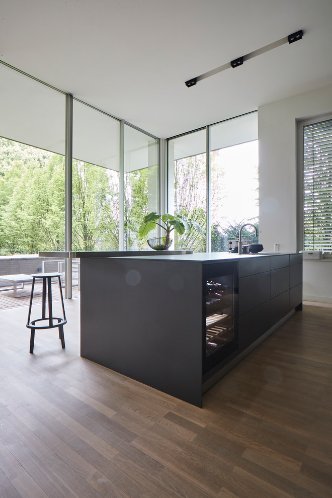 Inspiration for a large contemporary single-wall eat-in kitchen in Hamburg with flat-panel cabinets, black cabinets, black splashback, black appliances, light hardwood floors, with island, beige floor, black benchtop, a single-bowl sink and concrete benchtops.