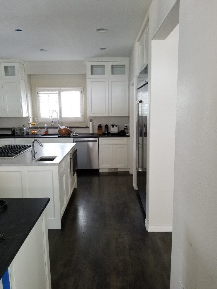 Inspiration for a large transitional u-shaped dark wood floor and brown floor eat-in kitchen remodel in Denver with an undermount sink, shaker cabinets, white cabinets, quartz countertops, stainless steel appliances, an island and black countertops