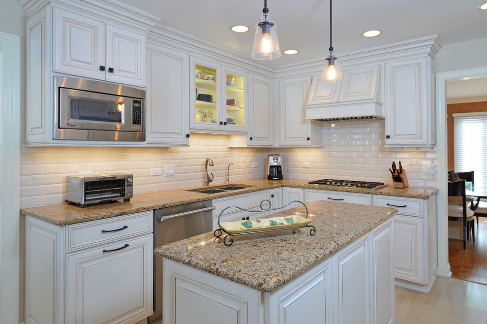 This is an example of a mid-sized transitional l-shaped eat-in kitchen in Chicago with an undermount sink, raised-panel cabinets, white cabinets, quartz benchtops, white splashback, subway tile splashback and stainless steel appliances.