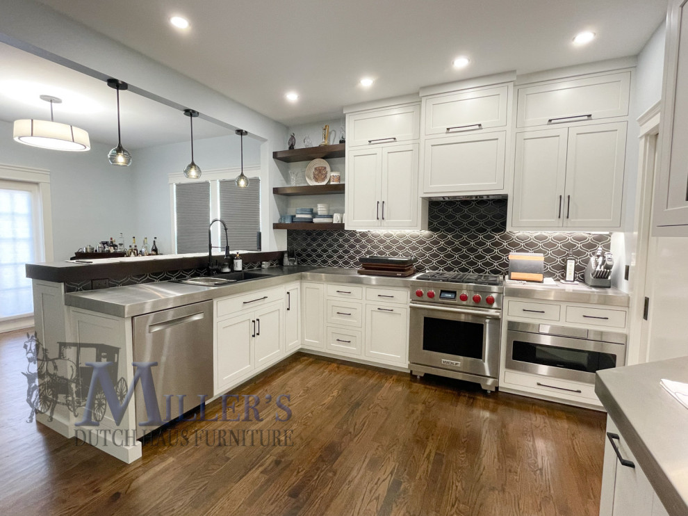 This is an example of a large classic u-shaped kitchen/diner in Tampa with white cabinets, stainless steel worktops, black splashback, black appliances, an island, brown floors and multicoloured worktops.