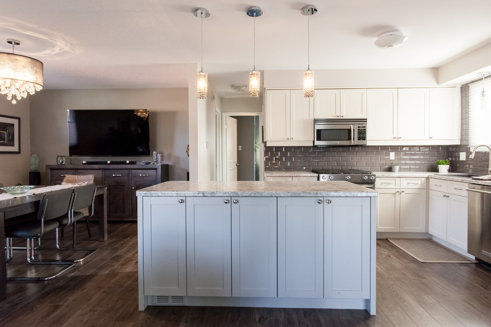 Mid-sized contemporary l-shaped eat-in kitchen in Toronto with a double-bowl sink, shaker cabinets, white cabinets, laminate benchtops, grey splashback, porcelain splashback, stainless steel appliances, laminate floors and with island.