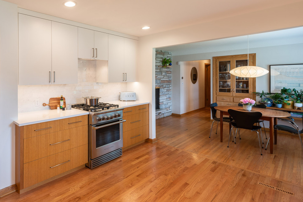 This is an example of a mid-sized midcentury galley kitchen pantry in Minneapolis with a single-bowl sink, flat-panel cabinets, light wood cabinets, quartz benchtops, white splashback, ceramic splashback, stainless steel appliances, medium hardwood floors, no island, brown floor and white benchtop.