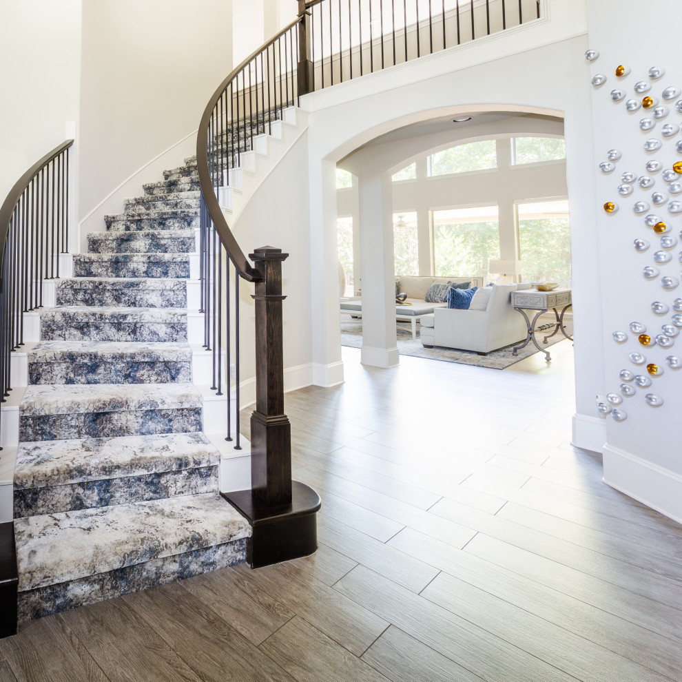На фото: изогнутая лестница в стиле неоклассика (современная классика) с ступенями с ковровым покрытием, ковровыми подступенками и деревянными перилами с