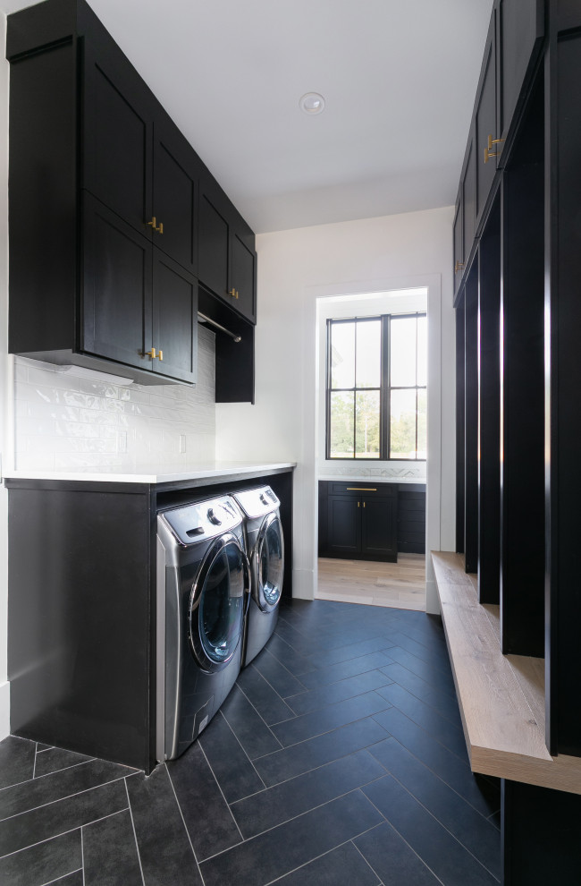 This is an example of an expansive country laundry room in Charleston with shaker cabinets, dark wood cabinets, wood benchtops, white splashback, subway tile splashback, white walls, porcelain floors, a side-by-side washer and dryer, black floor and white benchtop.
