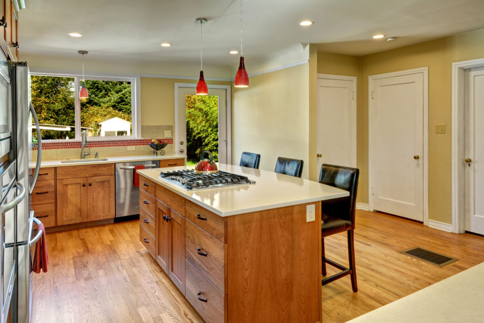 Example of a l-shaped medium tone wood floor and brown floor eat-in kitchen design in Seattle with an undermount sink, shaker cabinets, medium tone wood cabinets, red backsplash, mosaic tile backsplash, stainless steel appliances, an island and white countertops