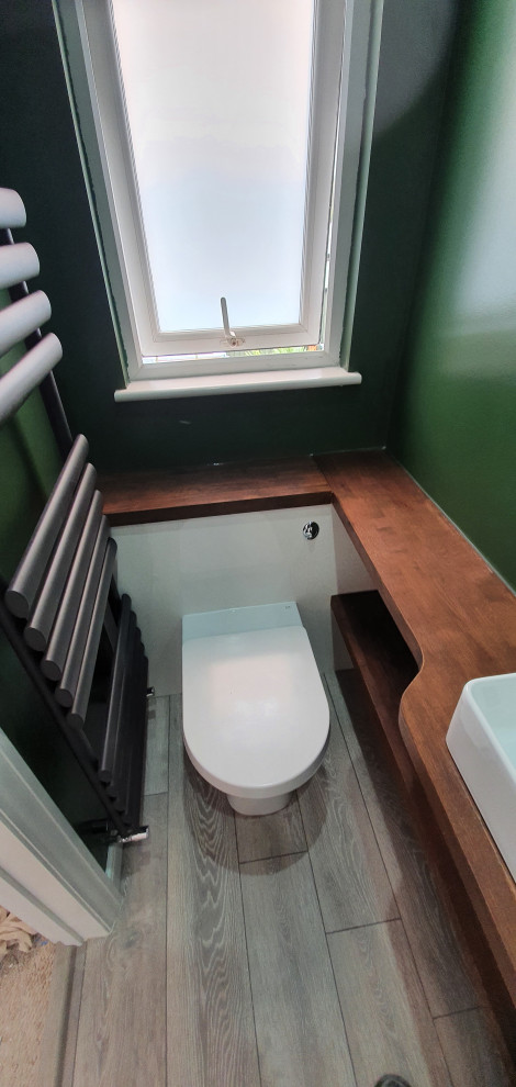 Modern inredning av ett litet brun brunt badrum, med släta luckor, vita skåp, en öppen dusch, en toalettstol med hel cisternkåpa, gröna väggar, laminatgolv, ett avlångt handfat, träbänkskiva, grått golv och dusch med gångjärnsdörr