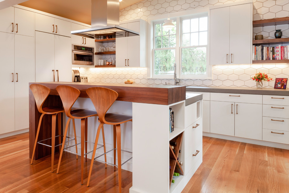 Inspiration for a mid-sized scandinavian l-shaped kitchen in Portland with flat-panel cabinets, white cabinets, concrete benchtops, white splashback, ceramic splashback, panelled appliances, medium hardwood floors, with island and grey benchtop.