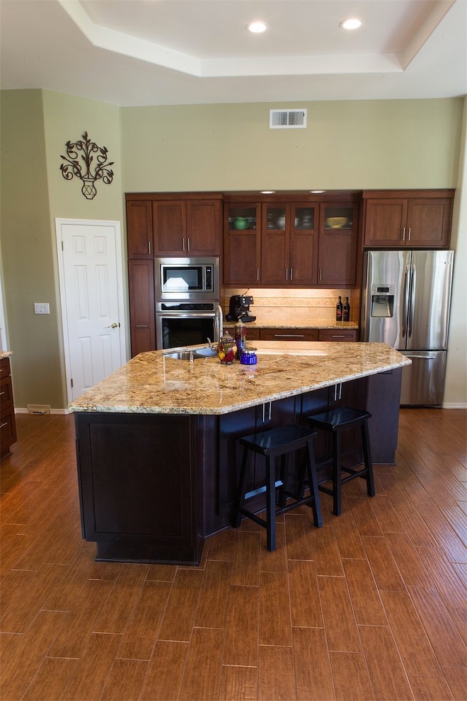 Kitchen - transitional l-shaped porcelain tile kitchen idea with an undermount sink, recessed-panel cabinets, medium tone wood cabinets, granite countertops, beige backsplash, stone tile backsplash, stainless steel appliances and an island