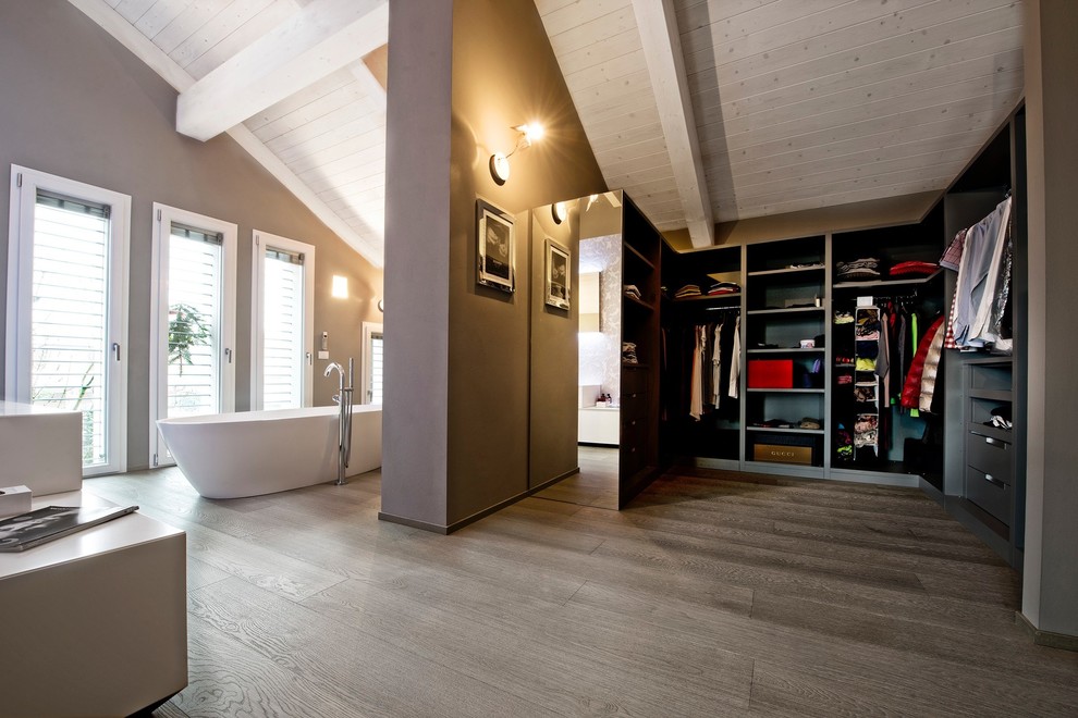This is an example of a contemporary gender-neutral walk-in wardrobe in Milan with open cabinets, grey cabinets, medium hardwood floors and brown floor.