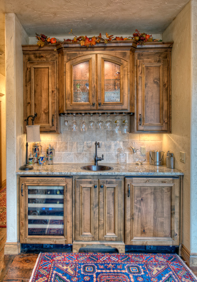 Mid-sized traditional single-wall wet bar in Other with a drop-in sink, recessed-panel cabinets, medium wood cabinets, granite benchtops, beige splashback, dark hardwood floors and travertine splashback.