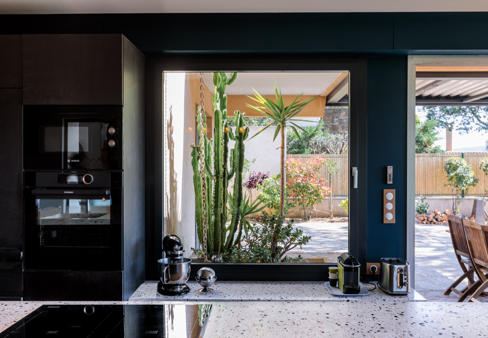Photo of a mid-sized contemporary galley open plan kitchen in Marseille with an integrated sink, glass-front cabinets, black cabinets, terrazzo benchtops, black appliances, cement tiles, with island, blue floor and blue benchtop.
