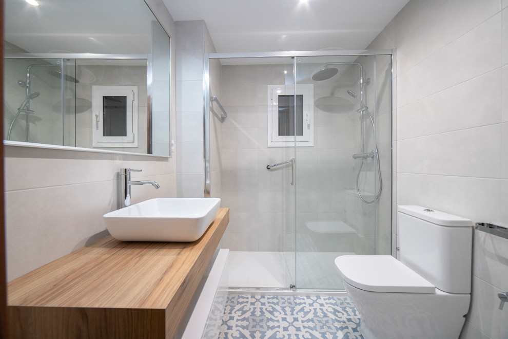 Design ideas for a mid-sized contemporary master bathroom in Barcelona with flat-panel cabinets, dark wood cabinets, a curbless shower, a one-piece toilet, white tile, ceramic tile, ceramic floors, a vessel sink, wood benchtops, blue floor, a sliding shower screen, brown benchtops, an enclosed toilet, a single vanity and a floating vanity.