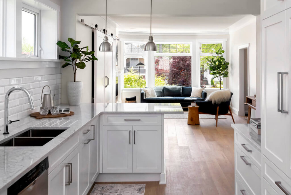 Inspiration for a mid-sized transitional galley medium tone wood floor and brown floor open concept kitchen remodel with a double-bowl sink, shaker cabinets, white cabinets, quartz countertops, white backsplash, subway tile backsplash, stainless steel appliances, a peninsula and gray countertops