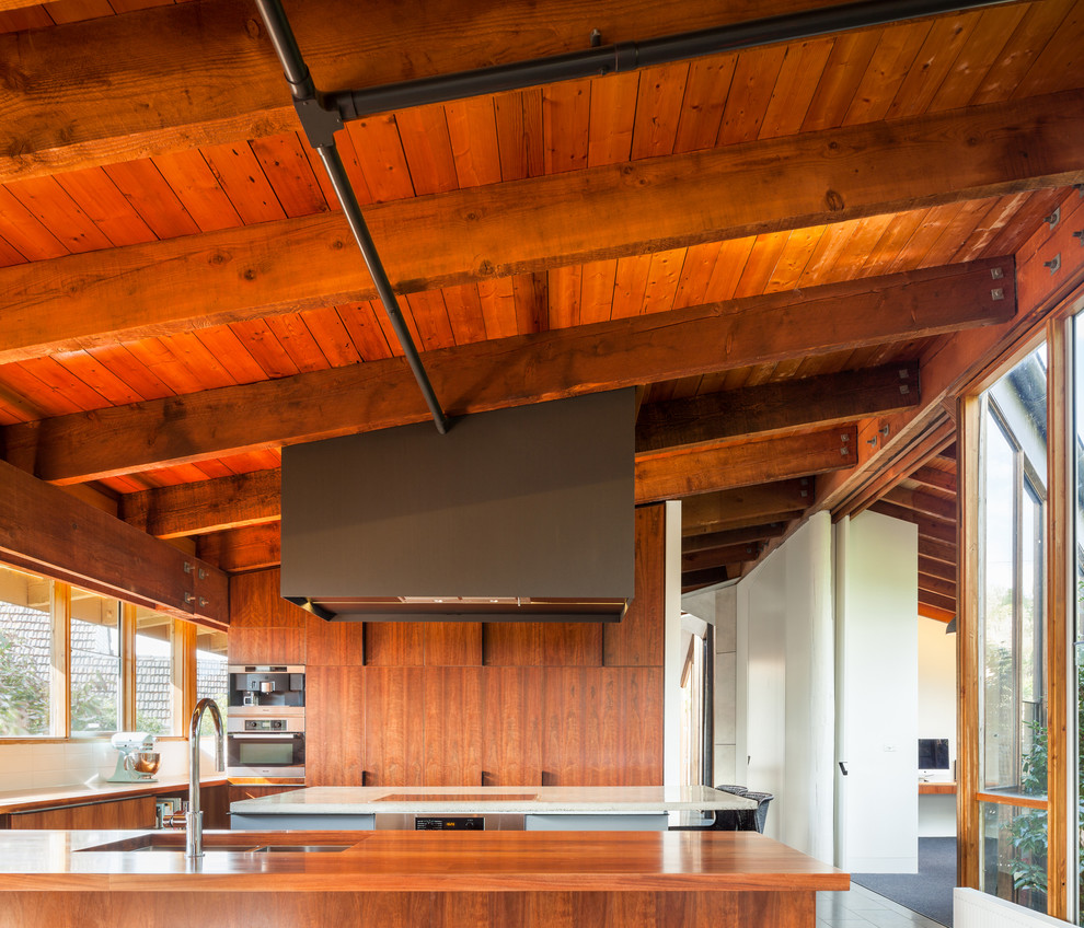 Large contemporary l-shaped open plan kitchen in Melbourne with a drop-in sink, dark wood cabinets, wood benchtops, white splashback, cement tile splashback, stainless steel appliances, ceramic floors and with island.