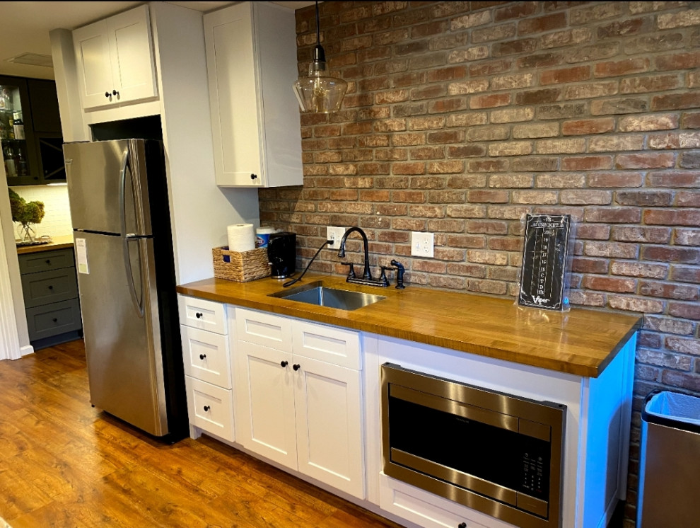 Photo of a mid-sized modern single-wall wet bar in Atlanta with an undermount sink, shaker cabinets, white cabinets, wood benchtops, multi-coloured splashback, brick splashback, light hardwood floors, brown floor and brown benchtop.