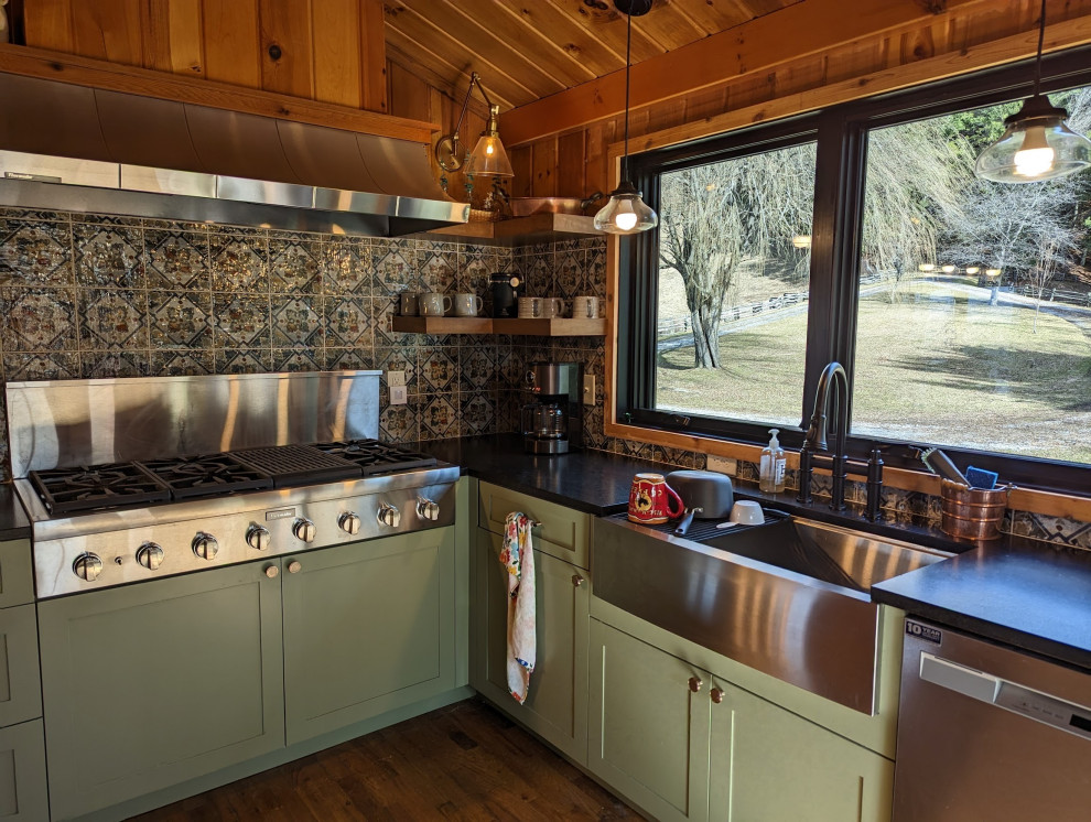 Mid-sized mountain style l-shaped medium tone wood floor, brown floor and wood ceiling eat-in kitchen photo with a farmhouse sink, shaker cabinets, green cabinets, granite countertops, multicolored backsplash, ceramic backsplash, stainless steel appliances and black countertops