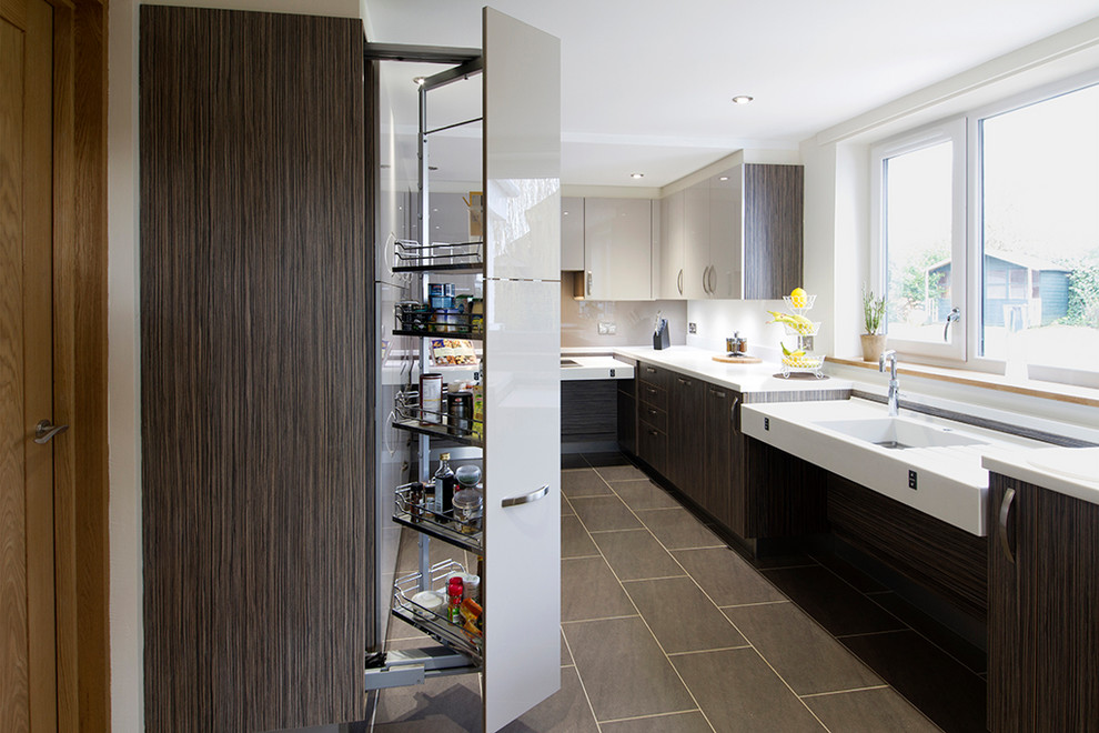 Small contemporary u-shaped open plan kitchen in Buckinghamshire with an integrated sink, flat-panel cabinets, beige cabinets, solid surface benchtops, beige splashback, glass sheet splashback, stainless steel appliances, porcelain floors, a peninsula and brown floor.