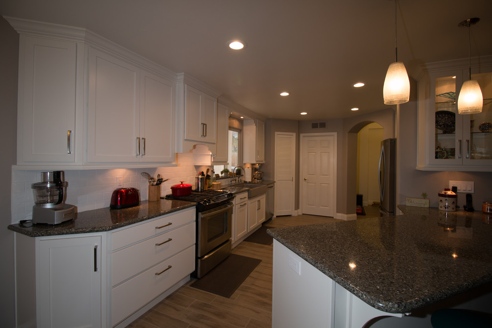 Mid-sized transitional galley porcelain tile open concept kitchen photo with a farmhouse sink, shaker cabinets, white cabinets, quartz countertops, white backsplash, subway tile backsplash and stainless steel appliances