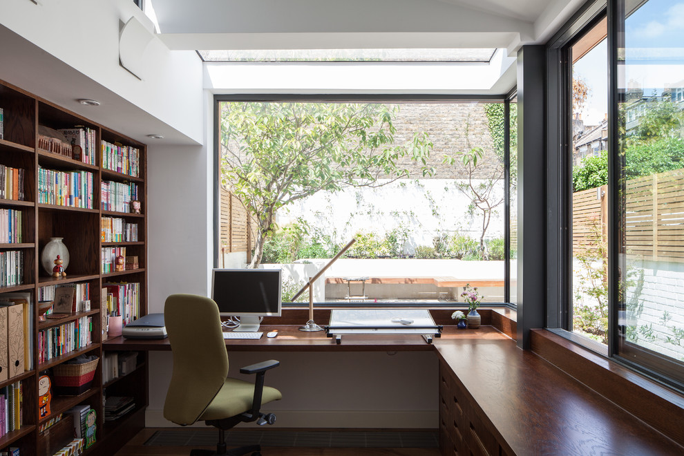 This is an example of a contemporary home office in London with white walls, dark hardwood floors, a built-in desk and brown floor.