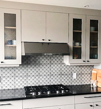 Large eclectic u-shaped laminate floor and brown floor eat-in kitchen photo with an undermount sink, glass-front cabinets, gray cabinets, quartz countertops, multicolored backsplash, ceramic backsplash, stainless steel appliances, an island and black countertops