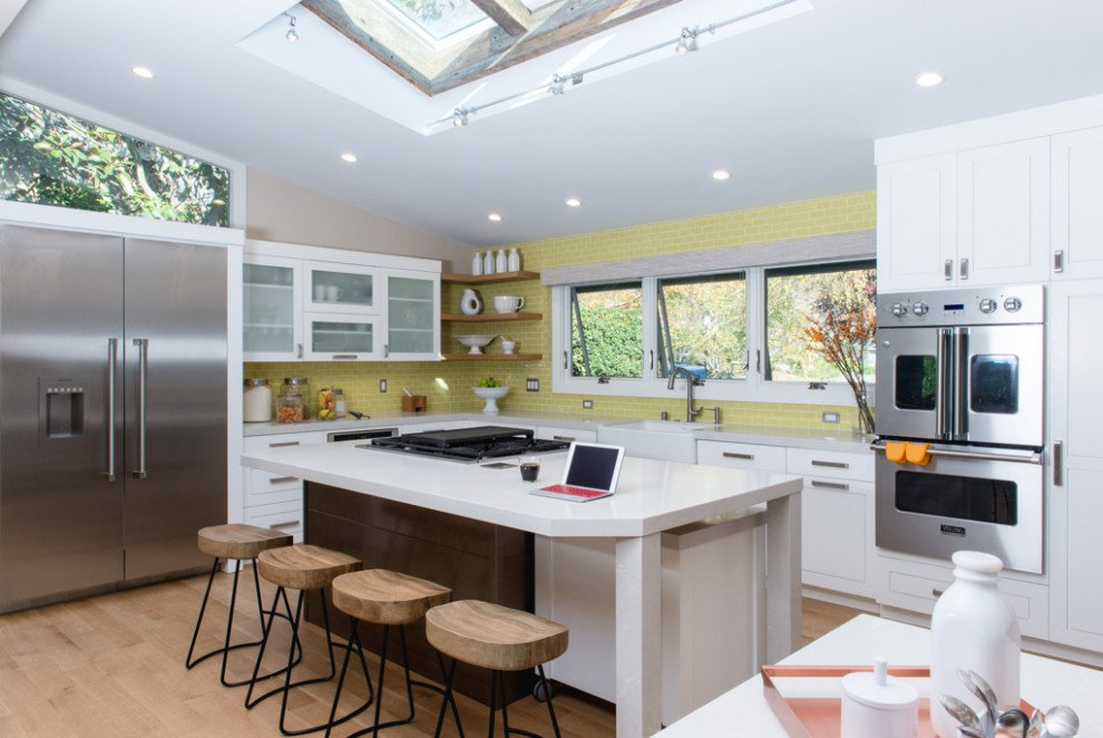 This is an example of a classic kitchen in San Francisco with a belfast sink, shaker cabinets, white cabinets, engineered stone countertops, green splashback, ceramic splashback, stainless steel appliances, light hardwood flooring, an island, beige floors, white worktops and a vaulted ceiling.