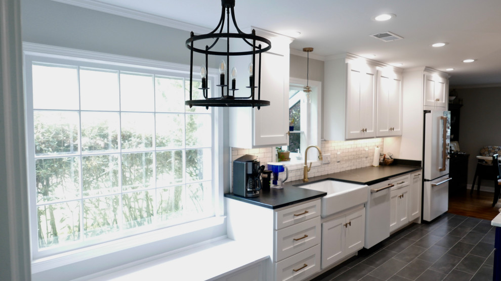Eat-in kitchen - mid-sized transitional galley porcelain tile and black floor eat-in kitchen idea with a farmhouse sink, shaker cabinets, white cabinets, soapstone countertops, white backsplash, subway tile backsplash, white appliances, an island and black countertops