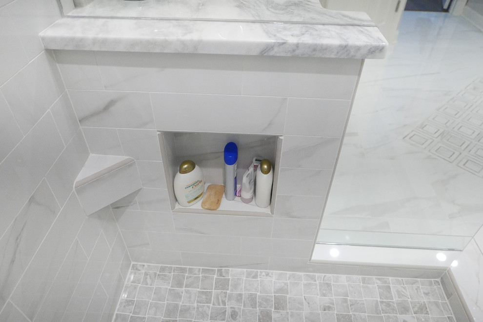 Large transitional master white tile and porcelain tile porcelain tile and white floor freestanding bathtub photo with shaker cabinets, white cabinets, a two-piece toilet, beige walls, an undermount sink, marble countertops, a hinged shower door and white countertops