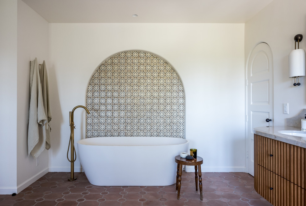 Inredning av ett amerikanskt grå grått en-suite badrum, med skåp i mellenmörkt trä, ett fristående badkar, flerfärgad kakel, klinkergolv i terrakotta, ett undermonterad handfat, marmorbänkskiva och brunt golv