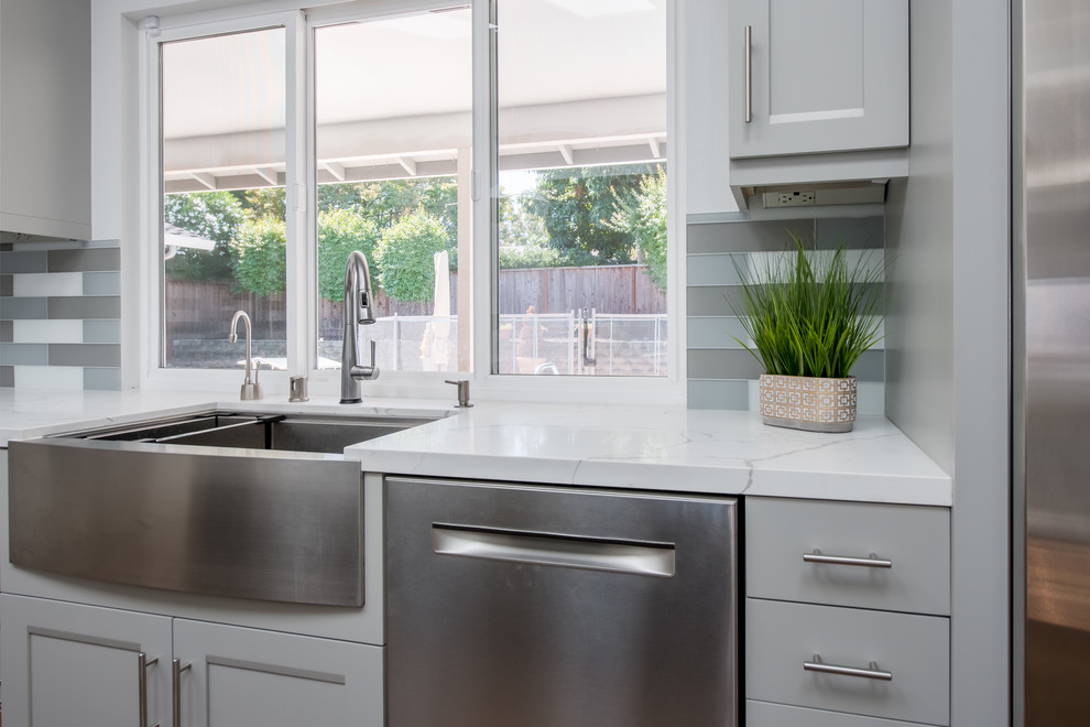 Mid-sized modern l-shaped eat-in kitchen in San Francisco with a farmhouse sink, shaker cabinets, grey cabinets, granite benchtops, grey splashback, glass tile splashback, stainless steel appliances, medium hardwood floors, with island, brown floor and white benchtop.