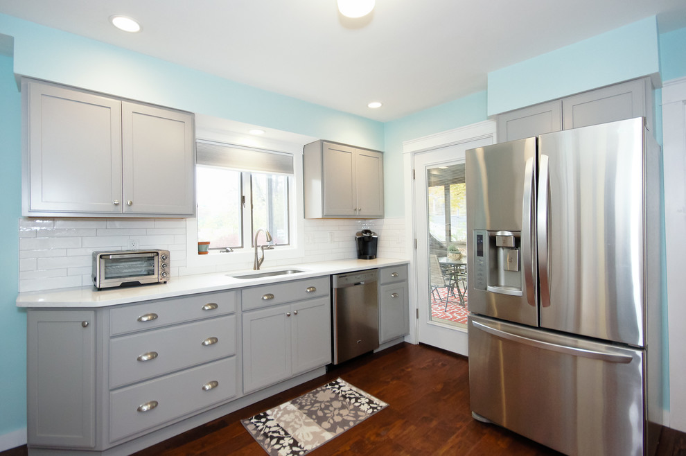 Inspiration for a mid-sized transitional galley medium tone wood floor and brown floor kitchen remodel in Boston with an undermount sink, shaker cabinets, gray cabinets, white backsplash, ceramic backsplash, stainless steel appliances and no island