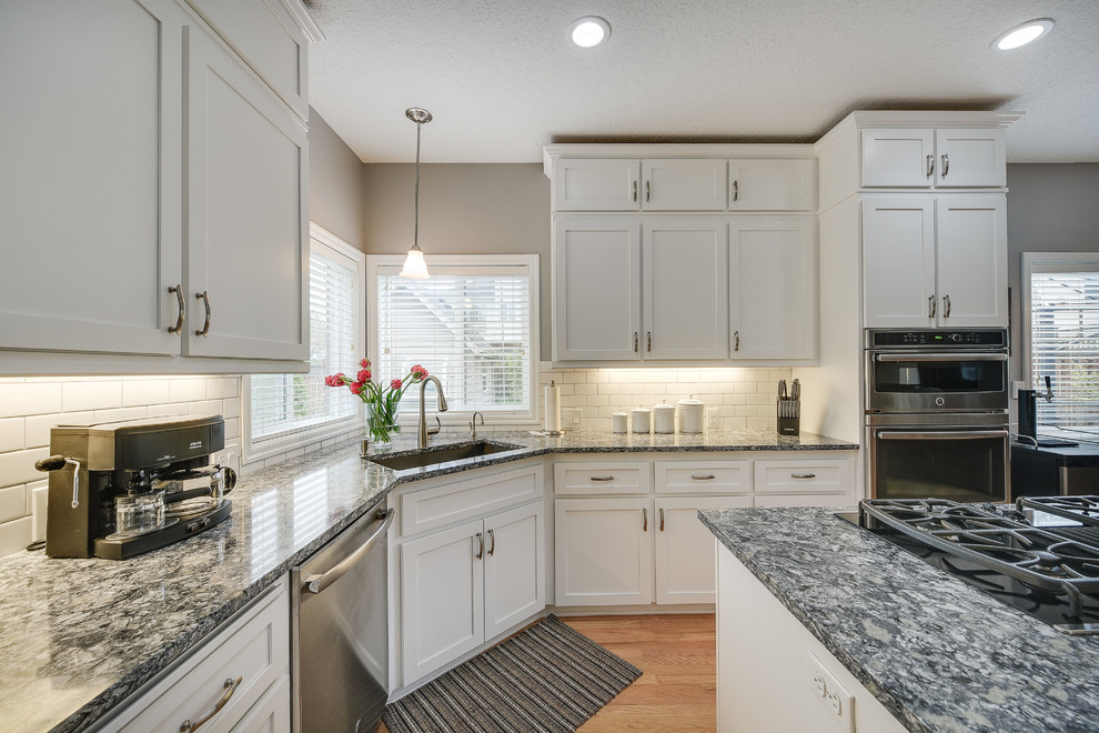 Inspiration for a mid-sized transitional l-shaped light wood floor and brown floor enclosed kitchen remodel in Portland with a drop-in sink, shaker cabinets, white cabinets, quartz countertops, white backsplash, subway tile backsplash, an island and stainless steel appliances