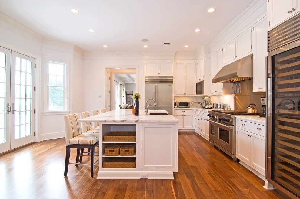 Inspiration for a large transitional l-shaped medium tone wood floor and brown floor eat-in kitchen remodel with a farmhouse sink, recessed-panel cabinets, white cabinets, marble countertops, white backsplash, marble backsplash, stainless steel appliances and an island
