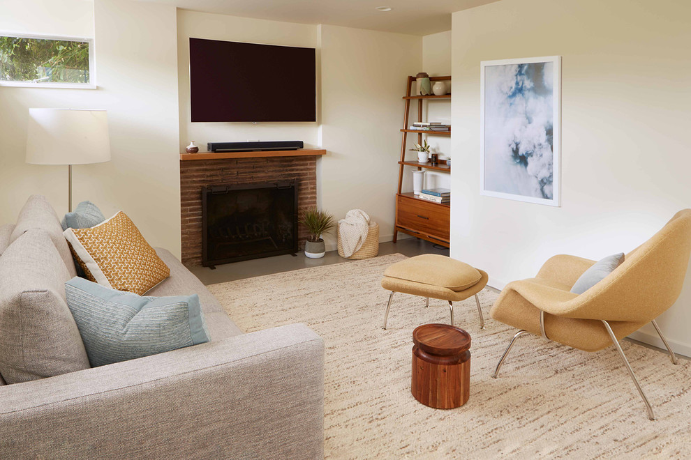 Small midcentury enclosed family room in Seattle with white walls, concrete floors, a standard fireplace, a brick fireplace surround, a wall-mounted tv and grey floor.