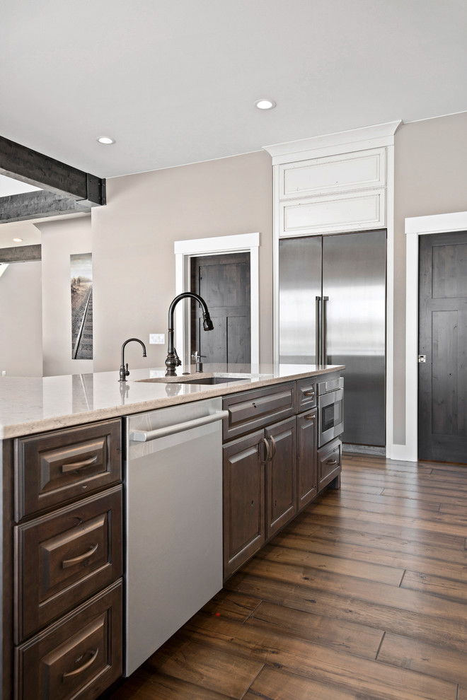 Inspiration for a large transitional l-shaped medium tone wood floor and brown floor eat-in kitchen remodel with an undermount sink, raised-panel cabinets, quartz countertops, beige backsplash, stone tile backsplash, stainless steel appliances, an island and beige countertops