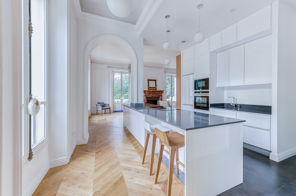 Modern inredning av ett stort grå grått kök, med en undermonterad diskho, vita skåp, bänkskiva i kvartsit, grått stänkskydd, rostfria vitvaror, klinkergolv i keramik, en köksö och grått golv