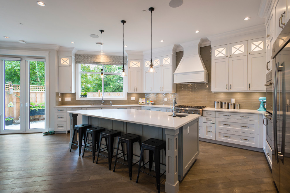 This is an example of a large transitional u-shaped open plan kitchen in Vancouver with an undermount sink, shaker cabinets, white cabinets, quartz benchtops, green splashback, glass tile splashback, stainless steel appliances, medium hardwood floors and with island.