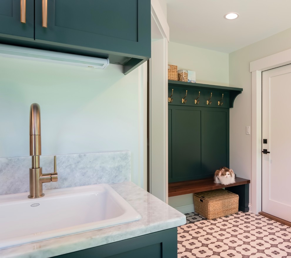 This is an example of a transitional l-shaped utility room in New York with a drop-in sink, shaker cabinets, green cabinets, granite benchtops, grey walls, ceramic floors, a side-by-side washer and dryer, white floor and white benchtop.