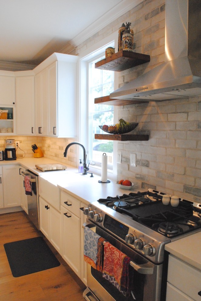 Eat-in kitchen - transitional light wood floor eat-in kitchen idea in Baltimore with a farmhouse sink, flat-panel cabinets, white cabinets, quartz countertops, white backsplash, stone tile backsplash, stainless steel appliances and an island