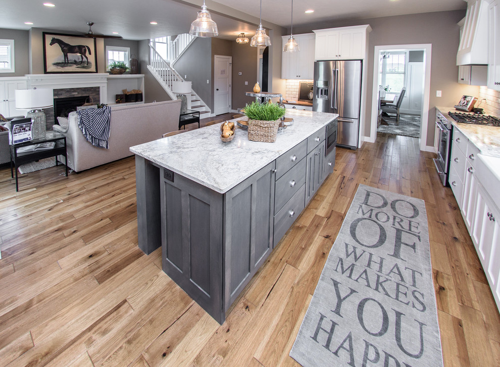 Open concept kitchen - mid-sized transitional u-shaped light wood floor and brown floor open concept kitchen idea with a farmhouse sink, shaker cabinets, gray cabinets, marble countertops, white backsplash, subway tile backsplash, stainless steel appliances and an island